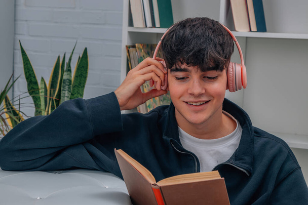 young man at home reading book and listening to music with headphones - Foto, Imagem