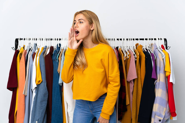Young Uruguayan blonde woman in a clothing store shouting with mouth wide open to the lateral - Foto, afbeelding