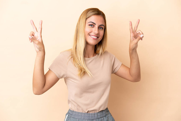 Blonde Uruguayan girl isolated on beige background showing victory sign with both hands - Foto, Imagem