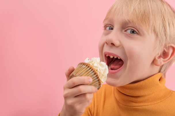 Portrait close up boy wants to eat cupcake. Blond child with muffin in his hands on pink background. Copy space. - Fotoğraf, Görsel