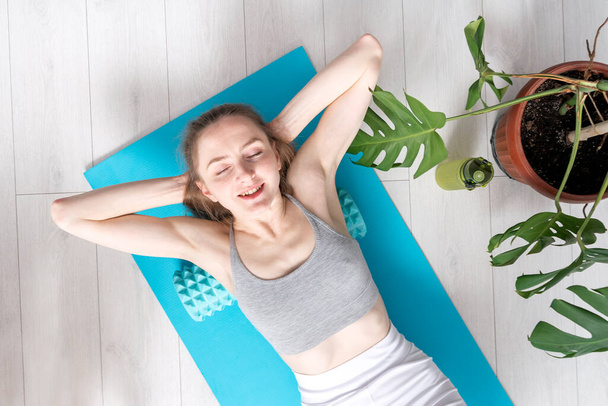 Mooie ontspannen gezonde vrouw doet een oefening met schuimroller op haar rug. Zelfmyofasciale massage thuis. - Foto, afbeelding