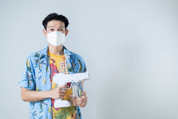 Mladý asijský muž v lékařské masce drží zbraň na sprej dezinfekční, Songkran Festival v Thajsku, pod covid-19 preventivní opatření, Kopírovat prostor. - Fotografie, Obrázek