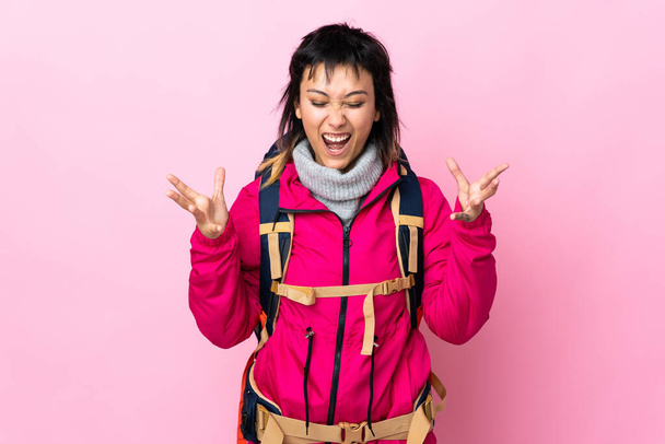 Junges Bergsteigermädchen mit großem Rucksack über isoliertem rosa Hintergrund unglücklich und frustriert über etwas - Foto, Bild