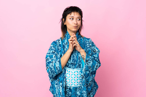 jonge vrouw dragen kimono over geïsoleerde blauwe achtergrond plannen iets - Foto, afbeelding
