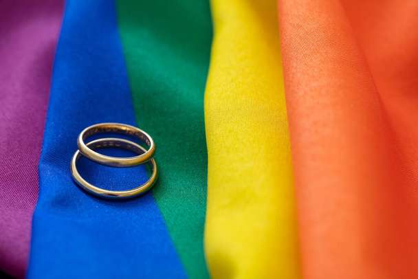 Homosexuelle Ehe. Paar goldene Ringe auf regenbogenfarbenem Textil mit Falten, Nahsicht. Kopierraum. - Foto, Bild