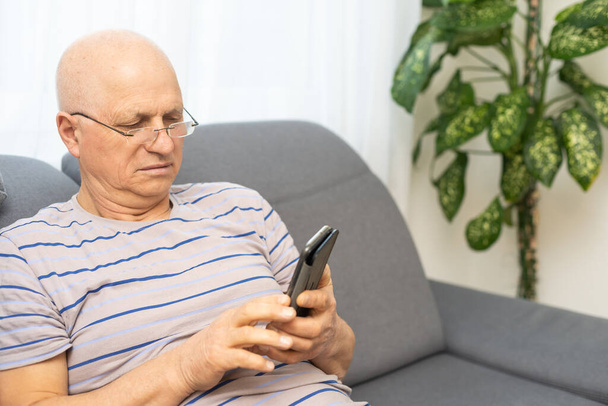 Hombre mayor charlando en un teléfono móvil mientras se relaja en un sofá en su sala de estar
 - Foto, imagen