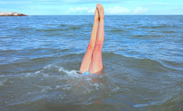 Uzun sıska bacaklı, yaz aylarında kafası denizin altında olan genç bir kız. - Fotoğraf, Görsel