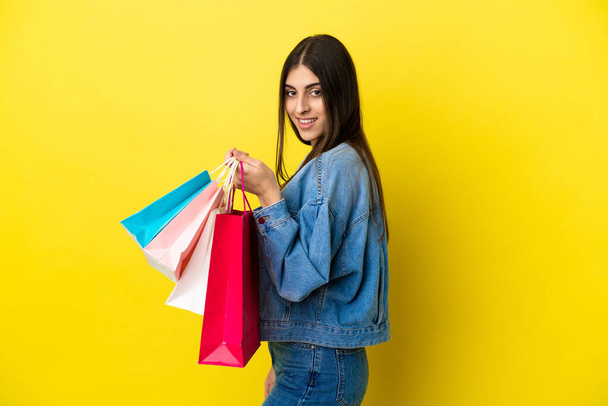 Junge kaukasische Frau isoliert auf blauem Hintergrund mit Einkaufstaschen und lächelnd - Foto, Bild