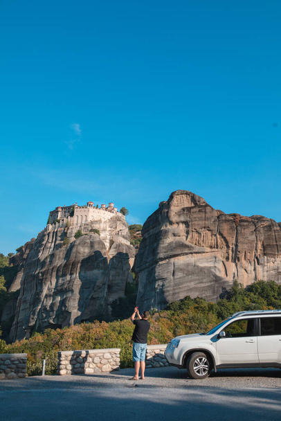 Griechenland Auto-Reisekonzept. Mann steht neben Geländewagen und betrachtet Meteora-Kloster im thessalischen Gebirge - Foto, Bild