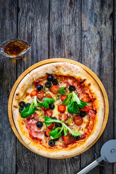 Circle prosciutto pizza with mozzarella, pork ham and black olives on wooden table  - Foto, afbeelding