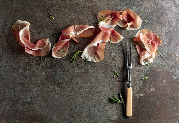 Prosciutto with rosemary on an old stone background. Traditional Mediterranean snack. Top view. - Photo, Image