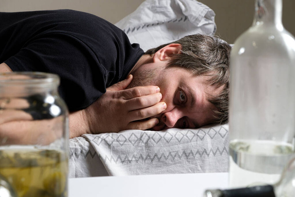 Um homem bêbado deita-se na cama, com as mãos na cabeça. Ressaca, delírio alcoólico. - Foto, Imagem