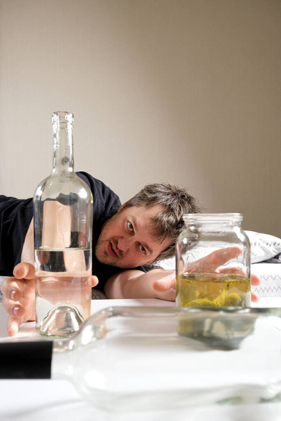 Ein betrunkener Mann mit Alkoholsucht nimmt eine Flasche Wodka und Sole mit eingelegten Essiggurken. - Foto, Bild