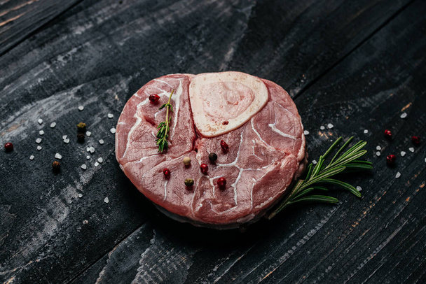 Raw beef meat osso buco shank steak with herbs and spices on dark background. banner, menu, recipe place for text, top view. - Foto, afbeelding