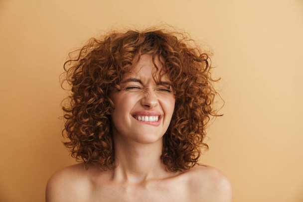 Half-naked ginger woman laughing while posing at camera isolated over beige background - Foto, afbeelding