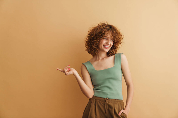 Young ginger woman laughing and pointing finger aside isolated over beige background - Photo, Image