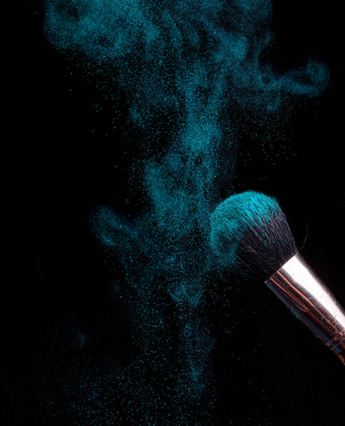 pinceau de maquillage avec poudre de différentes couleurs sur un fond sombre comme la poussière de l'espace - Photo, image