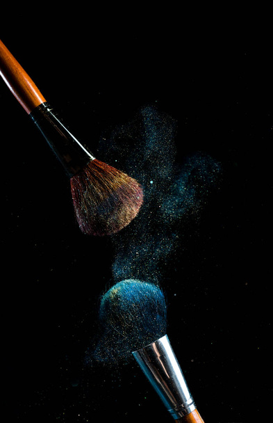 cepillo de maquillaje con polvo de diferentes colores sobre un fondo oscuro como el polvo del espacio - Foto, imagen