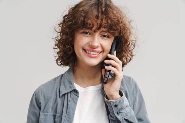 Young joyful woman smiling while talking on mobile phone isolated over white background - Foto, afbeelding