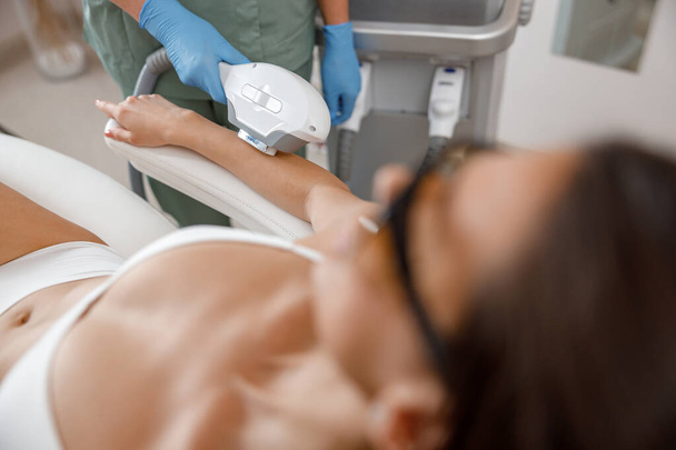 Primer plano del procedimiento de depilación en brazos con máquina ipl de un cosmetólogo profesional - Foto, Imagen