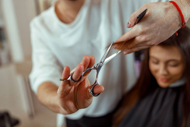 Κομμωτήριο κρατώντας ψαλίδι στα χέρια του και κόβοντας τα μαλλιά πελάτη - Φωτογραφία, εικόνα