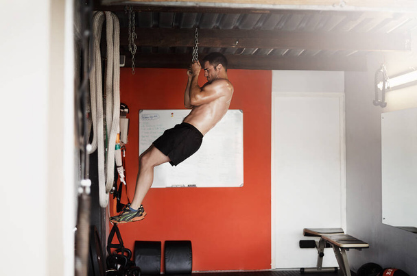Никогда не отпускай свои цели. Полнометражный снимок красивого и мускулистого молодого человека, делающего подтягивания, используя цепь в спортзале. - Фото, изображение