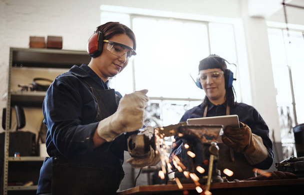 Working with metal. Cropped shot of two attractive young female artisans using an angle grinder in their workshop. - Foto, imagen