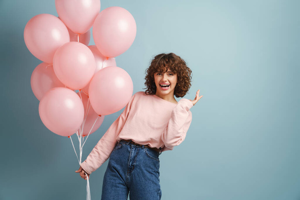 Young ginger happy woman smiling while posing with pink balloons isolated over blue background - Fotografie, Obrázek