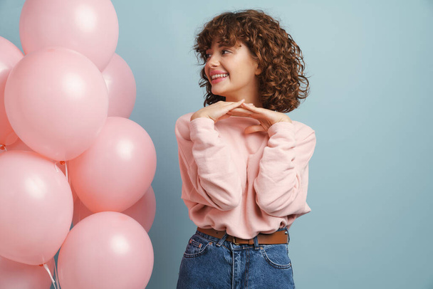 Young ginger happy woman smiling while posing with pink balloons isolated over blue background - Фото, зображення