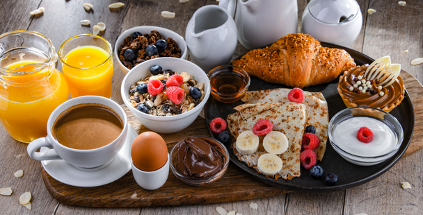 朝食にはコーヒー、オレンジジュース、パンケーキ、クロワッサン、シリアル、果物が添えられています。 - 写真・画像