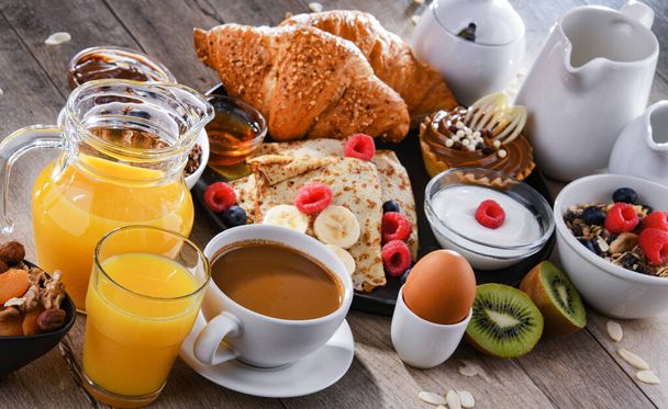 Desayuno servido con café, zumo de naranja, tortitas, croissants, cereales y frutas - Foto, imagen