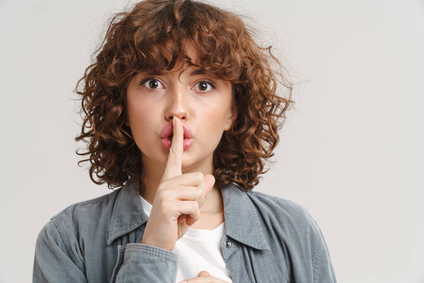 Ginger young woman looking and showing silence gesture at camera isolated over white background - Photo, image