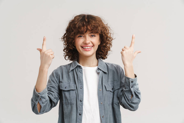 Young ginger woman in shirt smiling and pointing fingers upward isolated over white background - Foto, Imagem