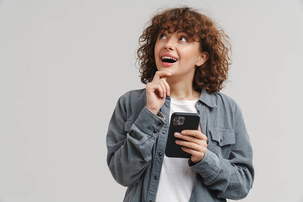 Young red excited woman exclaiming while using mobile phone isolated over white background - Φωτογραφία, εικόνα