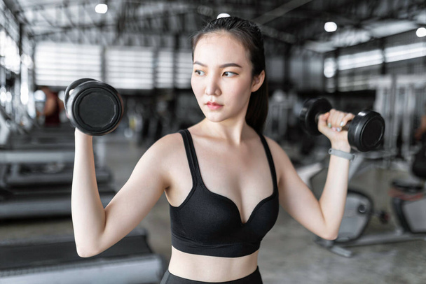 運動の概念暗いスポーツ服の健康な女性は彼女の髪を結ぶと重量挙げで動作します,上に2つの黒いダンベルを運ぶ. - 写真・画像