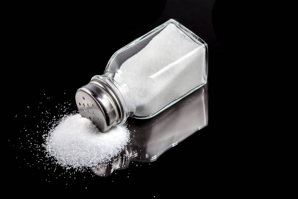 Salt shaker with spilled salt on a black background - Foto, afbeelding