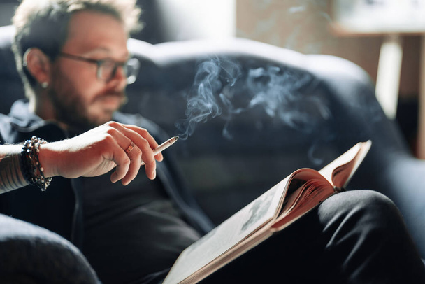 Estudante adulto lendo um livro na biblioteca da faculdade enquanto fuma - Foto, Imagem