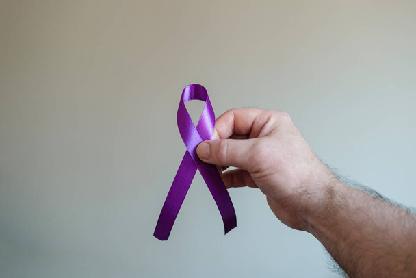 Mano derecha sosteniendo una cinta púrpura. Epilepsia, cáncer de páncreas y símbolo de Alzheimer. - Foto, imagen