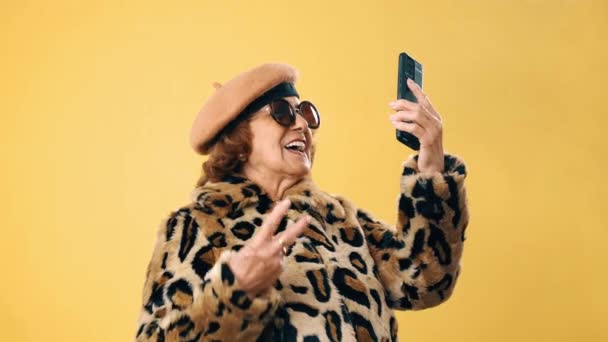 Stijlvolle senior vrouw glimlachen tijdens het hebben van een videogesprek of het opnemen van een video op haar mobiele telefoon. - Video