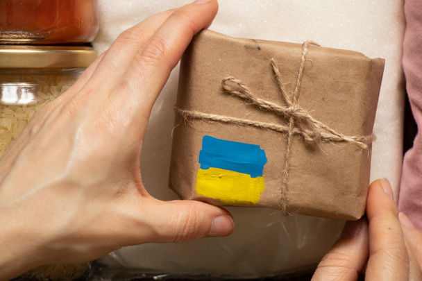 Krabička s namalovanou žlutomodrou vlajkou Ukrajiny v ruce ženy, humanitární pomoc Ukrajině od lidí - Fotografie, Obrázek