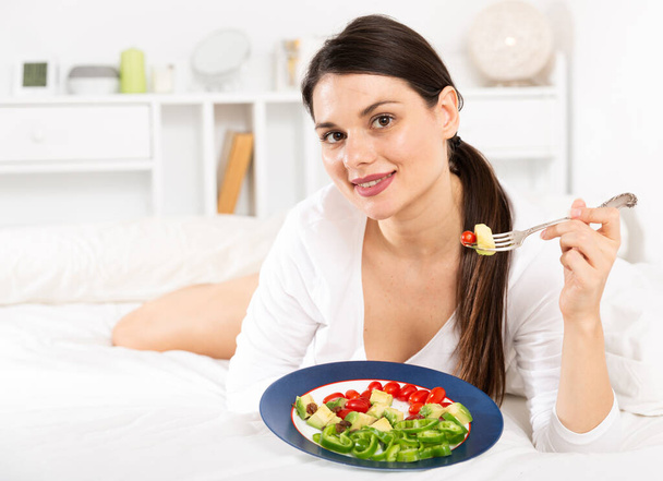 Portrait of brunette lady in white dress eating vegetable salad - Фото, изображение