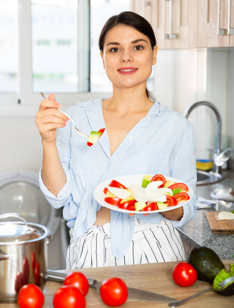 Woman tasting vegetable salad in kitchen - Foto, Imagen