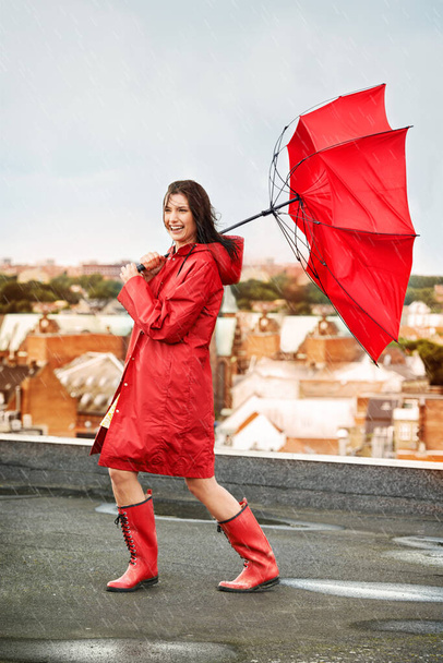 笑顔で嵐に直面しています。屋根の上で雨や風に打たれながら笑う若い女性. - 写真・画像