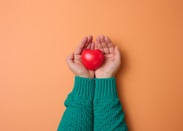 female hands holds red heart, orange background. Love and donation concept - Foto, afbeelding