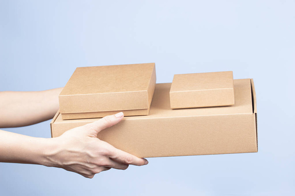 Stack of cardboard boxes in female hands. Blank brown parcel boxes on light blue background. Packaging, shopping, free shipping, delivery concept - Photo, Image