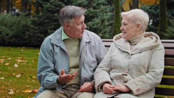 Usmívající se starší pár komunikovat sedět na lavičce muž gratulovat objímání manželka šťastný prarodiče strávit čas spolu venku starší žena sdílení dobré zprávy koncept silný zdravé rodinné vztahy - Záběry, video