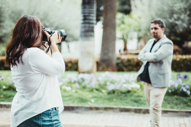 Selectieve focus op een vrouw die een foto neemt met een reflexcamera naar een zakenman in een park - Foto, afbeelding