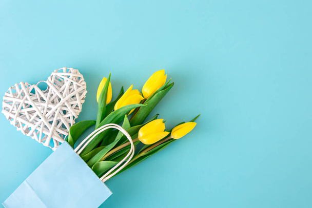 Flat lay blue background with yellow tulip flowers in a paper bag. - Photo, Image