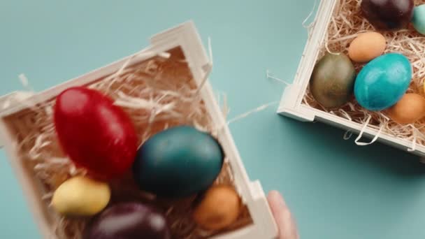 La mano está colocando una caja de huevos de Pascua en la mesa, fondo azul claro - Metraje, vídeo