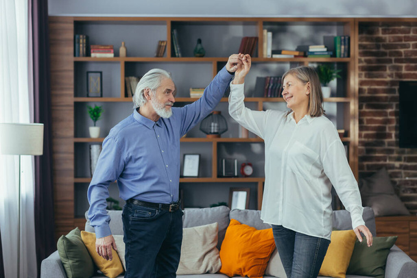 Happy cheerful senior married couple having fun at home. older family is dancing. Gray haired retirees rejoice moving active lifestyle. Old man and woman spend leisure time indoors listen to music - Foto, Imagen
